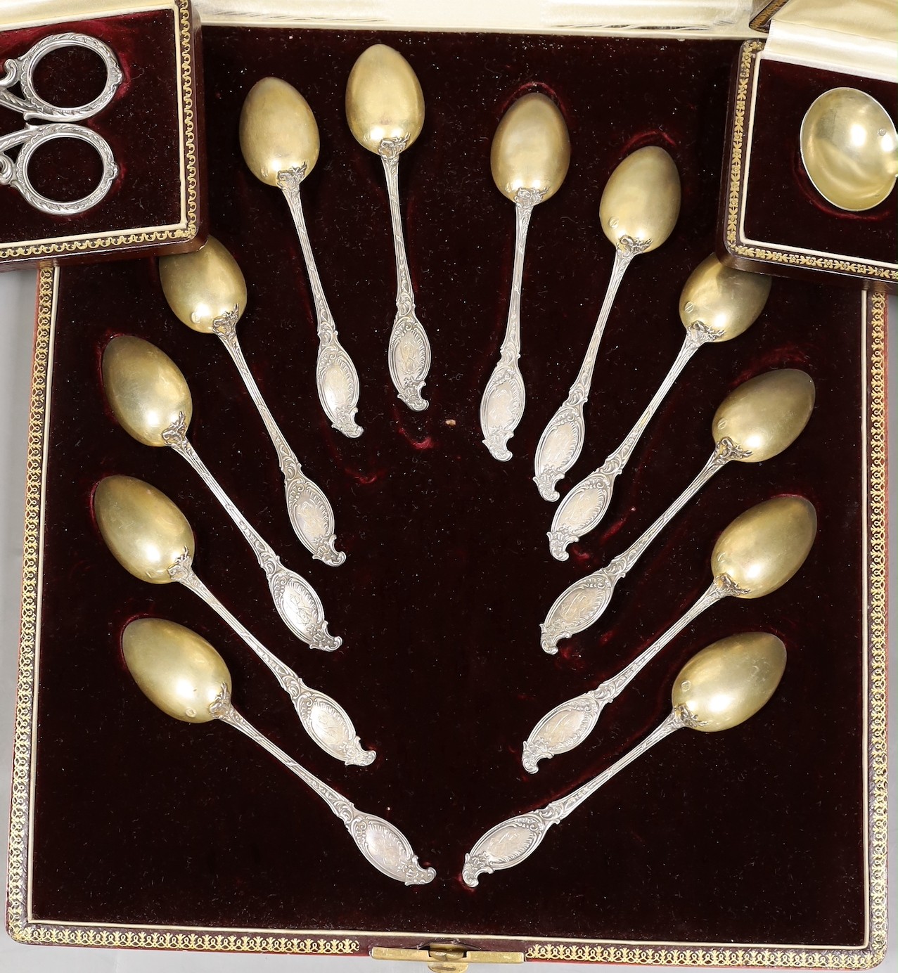 A cased set of twelve early 20th century French white metal fancy pattern teaspoons, a similar cased preserve spoon and a similar cased pair of white metal handled grape shears.